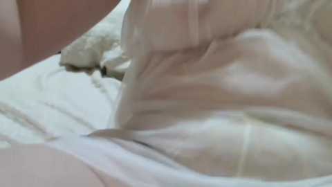 Media: Video of a person's arm and torso, lying on a white bed with a fluffy, cream-colored pillow. The skin tone is fair, and the background is soft and slightly blurred.