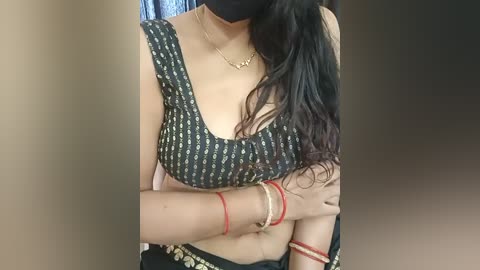 Media: Video of a South Asian woman with light brown skin, wearing a black blouse with gold pattern, black mask, and red bracelets.