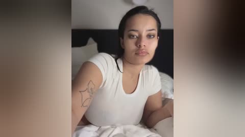 Media: Video of a young Asian woman with dark hair and medium skin tone lying on a bed, wearing a white t-shirt, with a star tattoo on her arm.