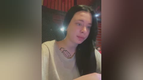 Media: A video of a young woman with long black hair, fair skin, and a light gray t-shirt, featuring a tattoo of a cartoon microwave on her chest. The background shows a dimly lit, brick-walled room.