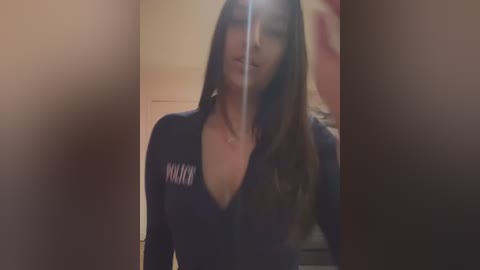 Media: A video of a woman with long brown hair, wearing a dark long-sleeved shirt with \"MAMA\" written on it, standing indoors. The image is blurry with a soft focus.