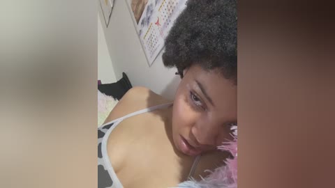 Media: A video of a young woman with a dark brown Afro hairstyle, wearing a black and white cow-print bra, lying on a pink feather pillow, with a calendar on the wall in the background.