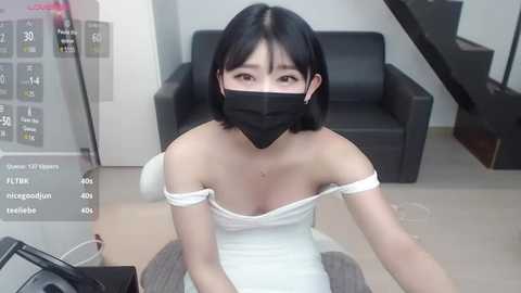 Media: A video of an East Asian woman with short black hair, wearing a white off-shoulder dress, black face mask, and sitting at a desk, with a virtual reality headset on.