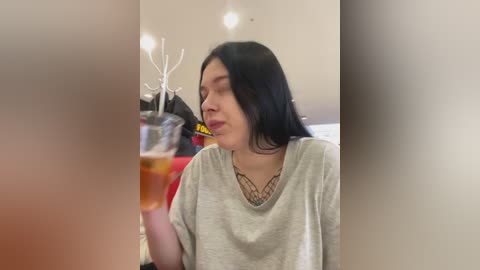 Media: A video of a young woman with long black hair and a gray t-shirt, sipping a glass of beer, wearing a decorative necklace.