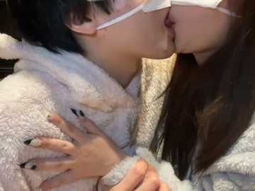 Media: Video of an Asian woman with short black hair, wearing glasses, kissing another woman's exposed breast, both in white bathrobes, hands intertwined.