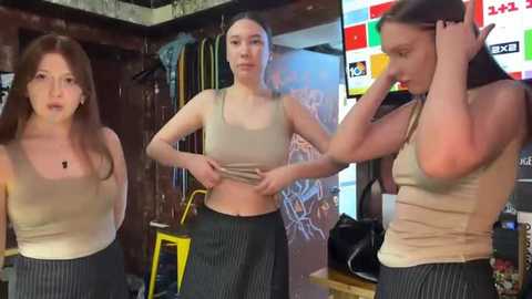 Media: Video of three young women in a messy room; one adjusting a tank top, another pulling down pants, and the third in a beige top, all in casual attire.