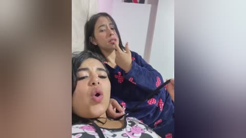 Media: Video: Two young women, one with light brown skin, black hair, wearing a blue nightgown, and the other with darker skin, black hair, and a similar nightgown, both appear to be in a state of arousal, captured in a bathroom setting.