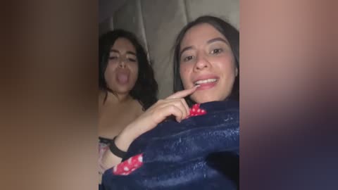 Media: Video of two young women, one with dark hair and one with light brown hair, making silly faces and sticking out their tongues, wearing dark blue robes.