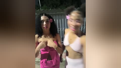 Media: Video of two women outdoors at night. One with dark curly hair, pink top, and exposed breasts; the other with dark hair, pink top, and white bra.