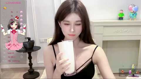 Media: Video of an Asian woman with long brown hair, wearing a black camisole, drinking from a glass, surrounded by cartoon characters in a minimalist room.