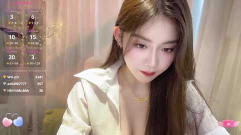 Media: Video of a young East Asian woman with long brown hair, fair skin, wearing a white button-up shirt, partially unbuttoned, with a gold necklace. Background shows a dimly lit room with a calendar app and social media icons.