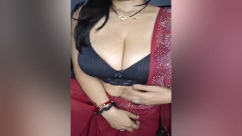 Media: Video of a South Asian woman with long black hair, wearing a black bra and red sari with sequins, and gold jewelry, standing indoors.