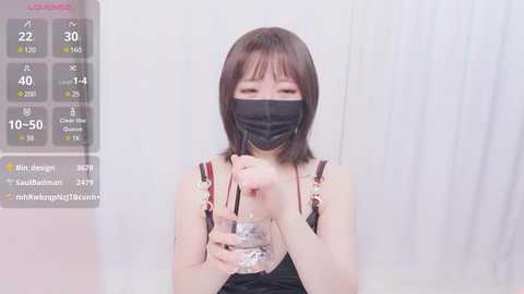 Media: A video of a young Asian woman with short brown hair, wearing a black mask, drinking water from a glass. She's in a room with white curtains and a digital overlay showing temperature and humidity.