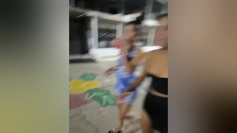 Media: A blurred video captures a young woman in a blue tank top and shorts, holding yellow and green balloons, standing next to a man in black. The background shows a dimly lit, possibly indoor setting with glass windows.