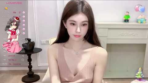 Media: A video of a young Asian woman with long, straight dark hair, wearing a beige sleeveless top, sitting indoors. Background includes a white fireplace, toys, and a pink doll on a table.