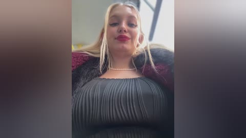 Media: A video of a blonde woman with fair skin and a slim physique, wearing a dark gray ribbed top and a maroon fur-trimmed jacket, sitting in a car.