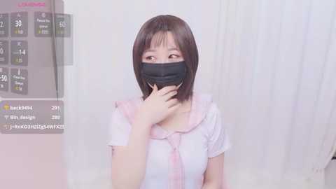 Media: A video of an East Asian woman with straight black hair, wearing a pink blouse, black face mask, and sitting in a white room. A digital overlay shows user statistics.