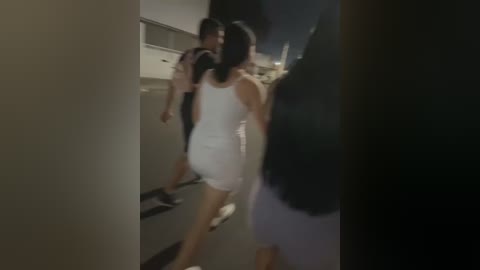 Media: A dimly lit video captures three people, two men and a woman, walking indoors. The woman, with long dark hair, wears a white dress. The setting appears to be a modern, possibly upscale, indoor space.