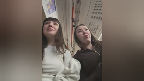 Media: A video shows two young women with long hair, one in a white sweater, the other in a black top, looking up thoughtfully in a subway train.