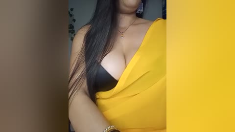 Media: A close-up video of a woman with long, straight black hair, wearing a yellow sari draped over a black bra, revealing her cleavage.