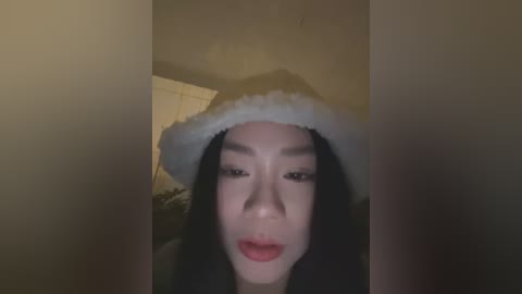 Media: Video of a young East Asian woman with fair skin, wearing a Santa hat and red lipstick, partially obscured by a shadowy background.