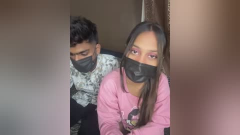 Media: Video of a young South Asian couple in a car, wearing black face masks, the woman with long dark hair in a pink hoodie, and the man in a patterned shirt.