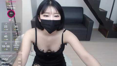 Media: A young East Asian woman with straight black hair, fair skin, and a slender physique, wearing a black lace bra and face mask, sits in a modern living room with a black couch and staircase.