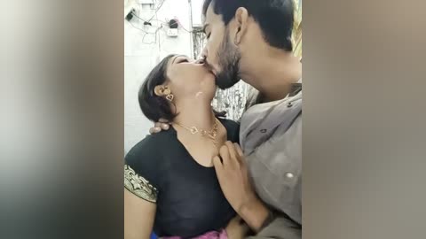 Media: Video of a South Asian couple passionately kissing in a dimly lit room, with the man wearing a grey shirt and the woman in a black blouse with gold earrings and a necklace.