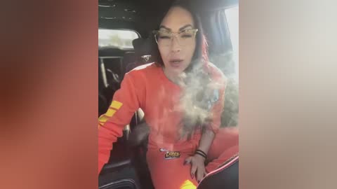 Media: A video of a woman in a red firefighter outfit with yellow stripes, smoking inside a car, eyes closed, exhaling smoke, wearing glasses.