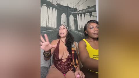 Media: Video of three Black women in a selfie, one in a revealing burgundy lace bodysuit, another in a yellow tank top, and a third in a black top. Background features a mural of the Brooklyn Bridge.