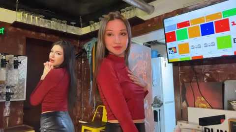 Media: Video of two young women in a cluttered bar, one wearing a red top and black shorts, the other in a red top, both looking seductively at the camera.