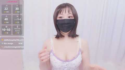 Media: A video of an Asian woman with short brown hair, wearing a black face mask, a white floral-patterned tank top, and a purple bralette. She stands against a white background, with a digital overlay displaying heart rate and other vitals.