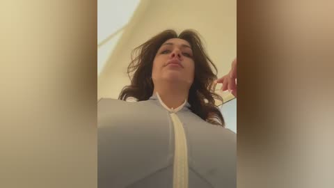 Media: Video of a curvy woman with long brown hair, wearing a tight, light blue shirt, captured from a low angle.