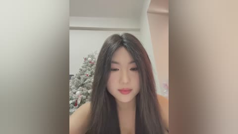 Media: Video of an Asian woman with long black hair, wearing red lipstick, standing indoors beside a decorated Christmas tree.