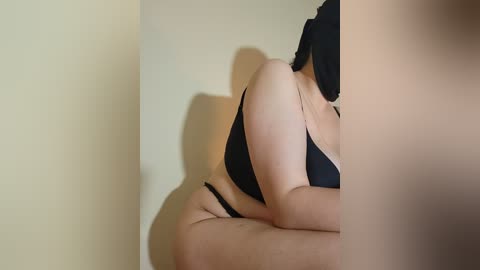 Media: Video of a curvy woman in black lingerie, sitting on a bed, her back and side prominently displayed. The room has beige walls, creating a soft, intimate ambiance.