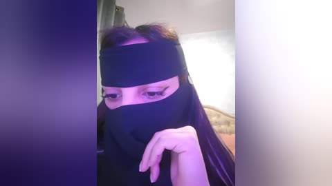 Media: A video of a woman with long dark hair, wearing a black veil and headband, her eyes visible, looking down. She is indoors, with a blurred background.