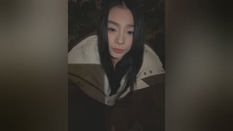 Media: Video of a young Asian woman with long black hair, wearing a dark coat, intently reading a book outdoors at night.