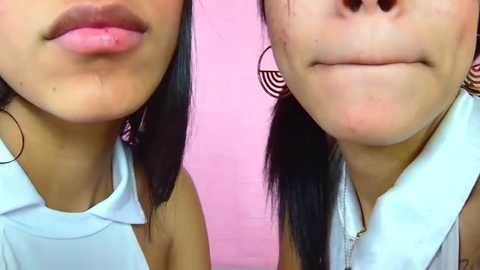 Media: Video of two Asian women with straight black hair, showing their faces and shoulders. One has light skin and full lips, while the other has a lighter complexion and closed lips. Background is a pink wall with a circular pattern.