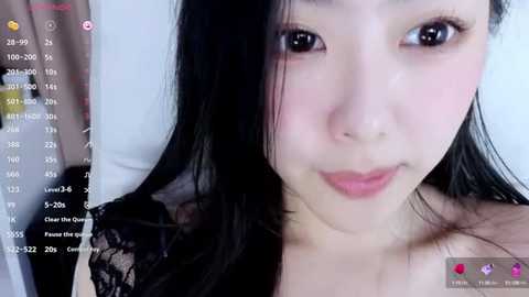 Media: A close-up video of an Asian woman with fair skin, black hair, and light makeup, wearing a black lace top. The background is blurred.