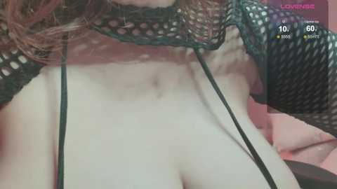 Media: A close-up video of a light-skinned woman with fair, wavy hair, wearing a black fishnet top, revealing her large breasts, and a black strap thong.