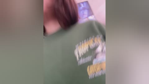 Media: Video of a person wearing a green shirt with yellow and white graphic design, partially obscured by blurred background.