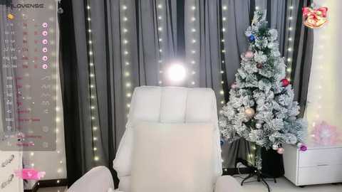 Media: Video of a modern, minimalist room with a white chair, Christmas tree, and calendar on a wall, adorned with fairy lights and festive ornaments.