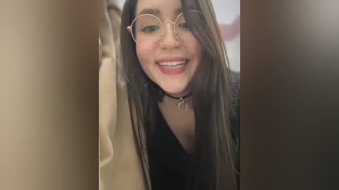 Media: A video of a smiling young woman with long dark hair, wearing glasses and a black top, peeking through a doorway.