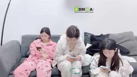 Media: Video of three Asian women in pajamas, watching smartphones on a gray couch, surrounded by white pillows and a DMOA watermark.