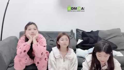 Media: Video of three East Asian women in pajamas on a gray sofa, with a \"DMCA\" watermark. The women appear to be in a casual, relaxed setting.