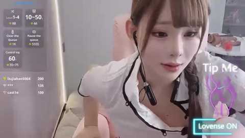 Media: Video of an Asian woman with long brown hair in a white blouse, wearing headphones, taken indoors. She has fair skin and a small bust. Background shows a computer screen displaying live streaming details.