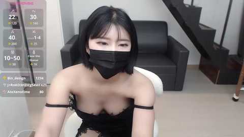 Media: A video of an Asian woman with short black hair, wearing a black mask, sitting in a modern room with a black couch and stairs.