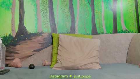 Media: A video of a cozy bedroom with a beige couch, a green pillow, and a green wall mural depicting a forest. The room has a soft, serene atmosphere.