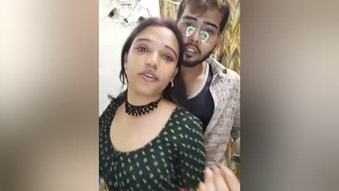 Media: A video of a young South Asian couple, with the woman wearing traditional attire and a black choker, and the man in a patterned jacket, standing in a rustic setting.