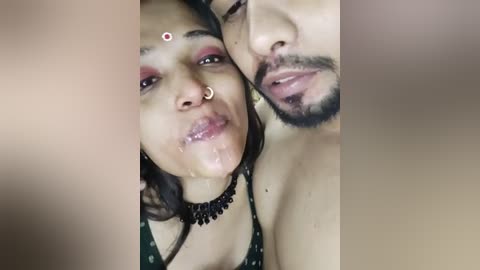 Media: Video of a light-skinned woman with a nose ring, heavy makeup, and a black necklace, kissing a bearded man, both with saliva on their lips.